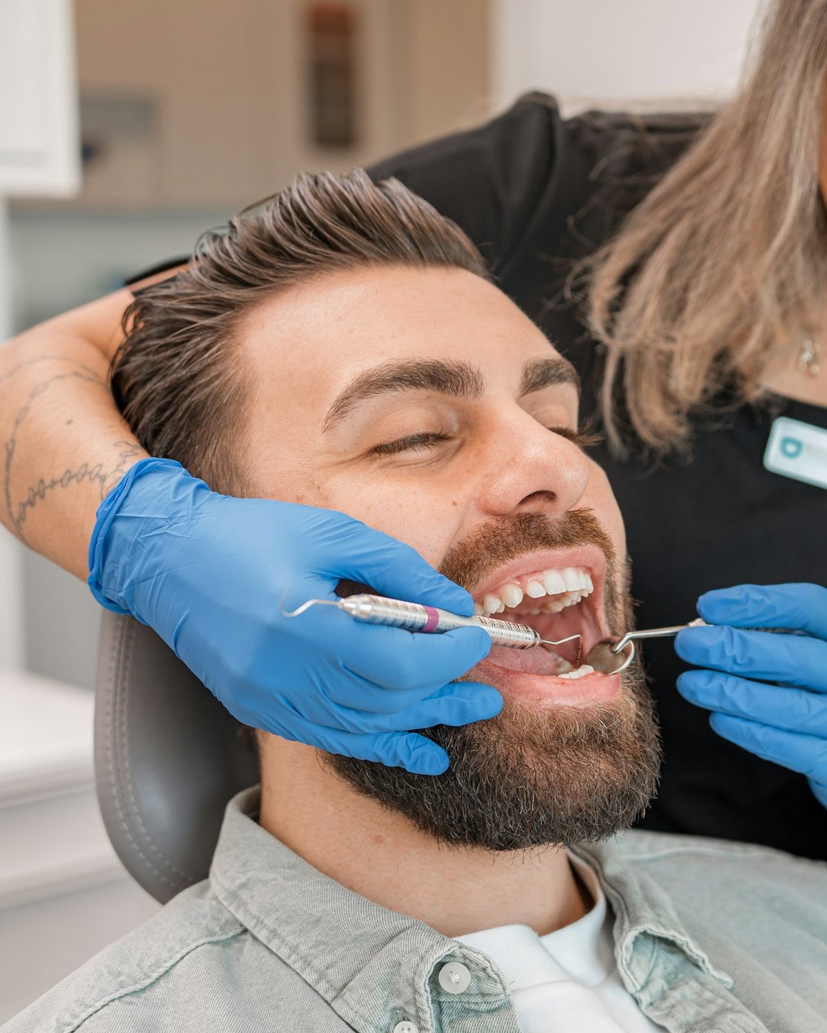 A dental professional in blue gloves examining a smiling patient's teeth